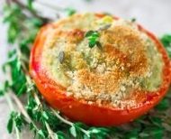 baked halved tomato with crusted parmesan on top, sitting on a bed of herbs